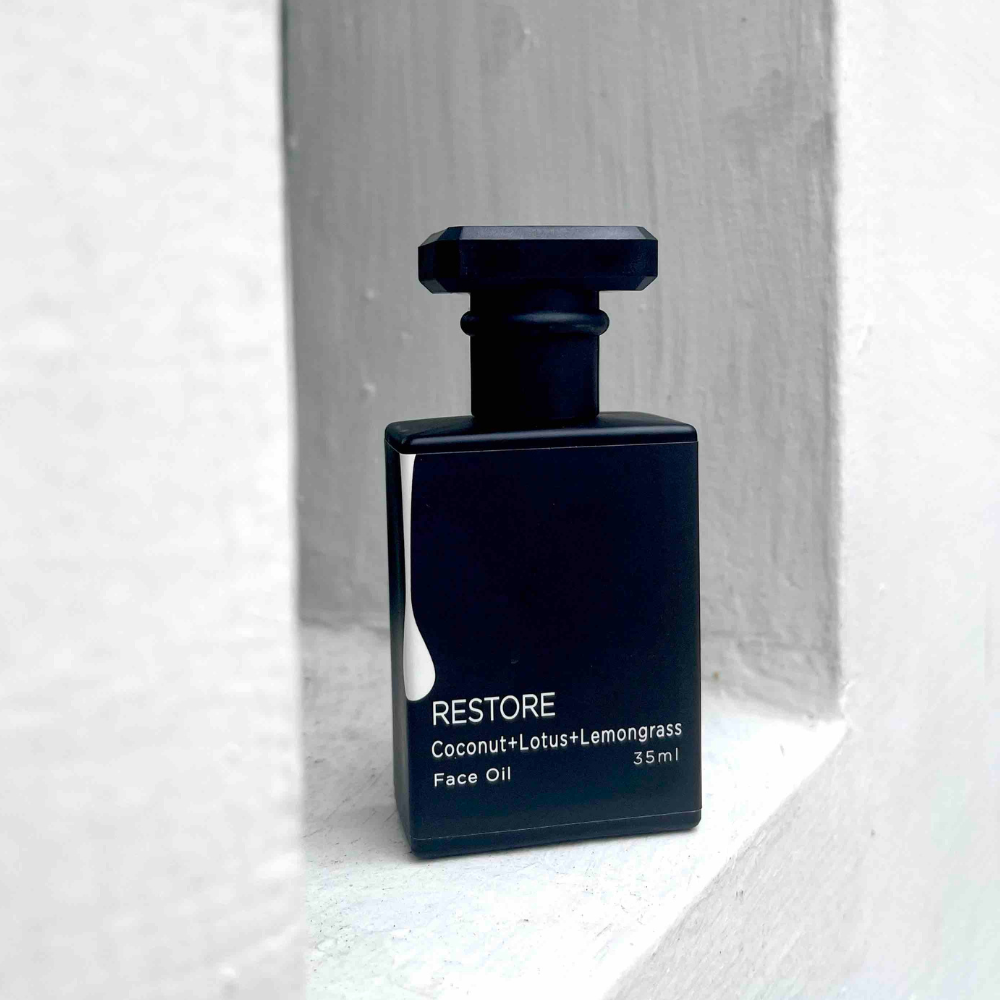 Black face oil bottle labeled 'Restore' on a light gray background